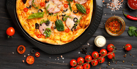 Pizza on a black baking dish on a dark wooden background, top view.