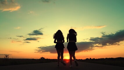 Athletic young women running along an asphalt road at sunset, leading healthy fitness lifestyle. Girls are training, running along road, teamwork of athletes. Slow motion. People run sun together, sky
