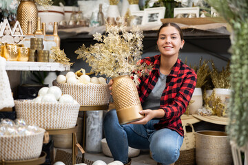 Positive young woman choosing decorative plant during christmastime in store.