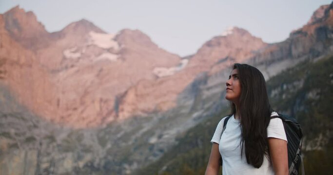 Latin woman backpacker looking up at the Swiss alps in the evening light