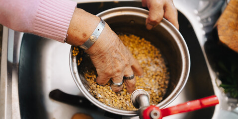 Elderly hands washing lentils in the kitchen.