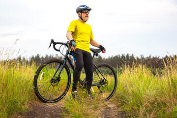 bearded man cyclist in yellow clothes is resting on a bicycle on the road in nature. sports, hobbies and entertainment for health
