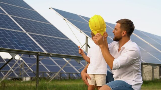 A father and his little son in a yellow helmet near the solar panels