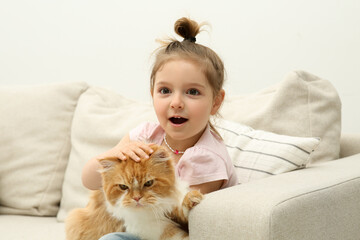 Cute little girl with adorable cat on sofa at home