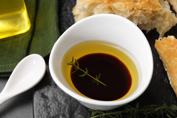 Bowl of organic balsamic vinegar with oil, thyme and bread on grey table, closeup