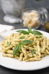 Plate of delicious trofie pasta with pesto sauce and basil leaves on grey wooden table, closeup