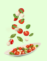 Fresh tomatoes. mozzarella cheese and basil leaves falling onto plate with Caprese salad against pale green background