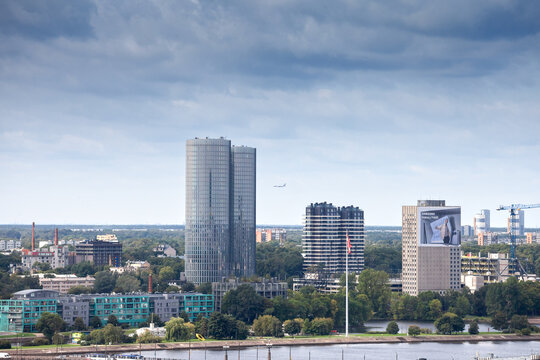 RIGA, LATVIA - AUGUST 22, 2023: Panorama of riga business district CBD, Kipsala, with a plane landing in the middle of a skyline of office buildings, high rise towers of skyscrapers.