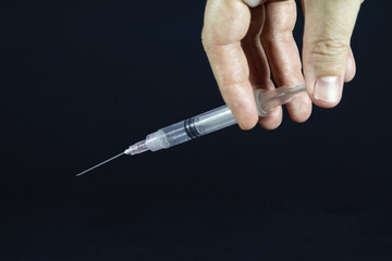 Selective blur on hand holding a syringe, medical syringe with a needle, ready for a drug medicine injection, isolated on a black background.