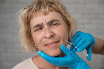 Doctor makes beauty injections in the face of an old caucasian woman. 