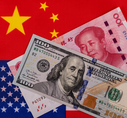 Banknotes in denominations of 100 US dollars and 100 Chinese yuan against the background of national flags