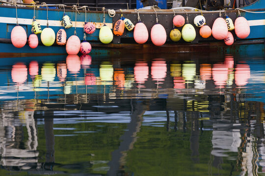 A Row Of Multicolored Buoys Hang Off The Side Of A Blue Fishing Boat, Sand Point Harbor, Southwestern Alaska, USA, Summer