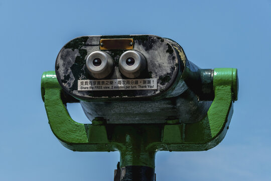 Green, Metal Public Binoculars Pointing Towards Blue Sky With Instructions Written In English And Chinese; Hong Kong