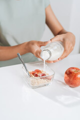 Close up of woman pouring milk into bowl with granola with grape