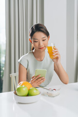 Obraz premium Happy young asian woman using mobile phone while having tasty breakfast in the kitchen