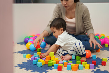 infant baby playing wooden block toy with mother in playpen