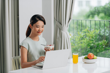 Beautiful young woman working on laptop while sitting at breakfast table in morning.