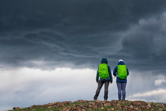 Close-up view, taken from behind, of two women wearing backpacks standing on a mountain ridge under a dark and foreboding sky near Whitehorse; Whitehorse, Yukon Territory, Canada