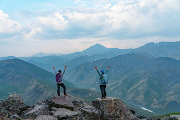 Two women standing on a rocky mountain top with their arms raised in the air in celebration, enjoying the view of the amazing scenery in Northern Yukon; Yukon Territory, Canada
