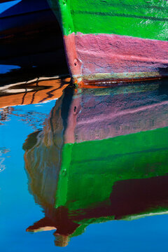 Detail of a small, wooden fishing boat moored to the shore with a mirror image reflection in the calm water in the coastal town of Getaria; Getaria, Gipuzkoa, Spain