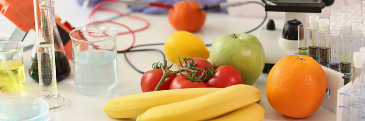 Fruits and vegetables with scientific equipment in laboratory, scientist takes notes in background.
