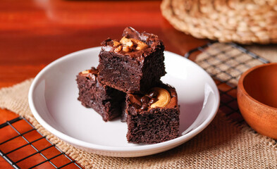 Chocolate pound cake. A piece of cake is cut into pieces and served with chocolate ganache cream. Brown wooden background. Dark mood.