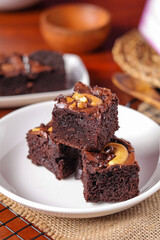 Chocolate pound cake. A piece of cake is cut into pieces and served with chocolate ganache cream. Brown wooden background. Dark mood.