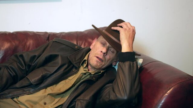 Man waking up from sleep. The mature man is woken up suddenly by a sound. He lifts his hat