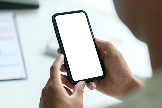 Rear view of young man sitting at his workspace and using smartphone. Blank screen for graphics display montage.