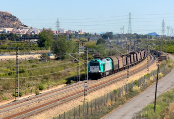 Obraz premium Freight train transports cargo in freight wagons. Diesel locomotive on railway in Spain. Train on the railroad against the backdrop of mountains and orange fields