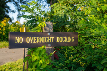 Weathered brown and gold wood sign on post, NO OVERNIGHT DOCKING.	