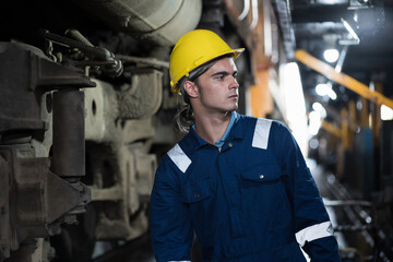 Male engineer maintenance locomotive engine, wearing safety uniform, helmet and gloves in locomotive repair garage. Male railway engineer repair train wheel in train garage
