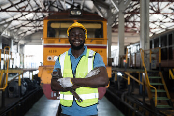 African American male engineer working with happy and smile in in locomotive repair garage. Portrait of male railway engineer repair train wheel in train garage