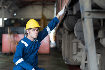 Male engineer maintenance locomotive engine, wearing safety uniform, helmet and gloves in locomotive repair garage. Male railway engineer repair train wheel in train garage