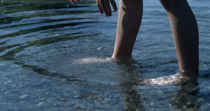 Child legs standing inside pond water in super slow motion 800 fps with ripples flowing, person in contact with nature