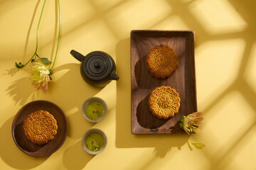 High view of delicious mooncakes on wooden trays decorated with black set of tea and flowers. Background for advertising product on Mid-autumn festival. Creative food design concept