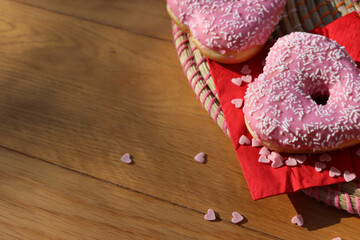 Pink glazed donuts in shape of a heart  on red napkin with heart sprinles on wooden table. Valentine’s day background