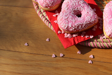 Pink glazed donuts in shape of a heart  on red napkin with heart sprinles on wooden table. Valentine’s day background