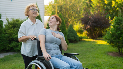 An elderly woman is carrying an adult daughter sitting in a wheelchair. Walk outdoors. 