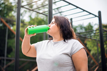 Woman with overweight drinking water on a sports field