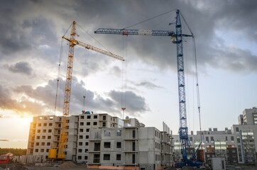 Fototapeta na wymiar Cranes and buildings under construction against the cloudy sunset sky