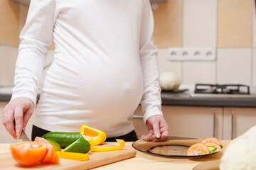 Closeup of Hands of Pregnant Woman Preparing Salad with Vegetables on Kitchen.