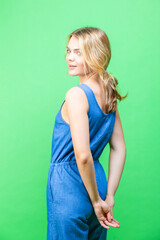 Caucasian Blond Girl In blue Dress Posing While Holding Hands Behind Back Over Summer Green Background.
