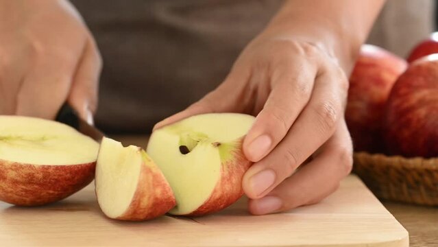 Red apple fruit with hand holding knife and cutting on wooden board