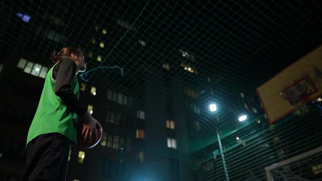 Side bottom view of fit man aiming at net standing on sports ground in night city. Concentrated focused Caucasian young sportsman playing game training outdoors