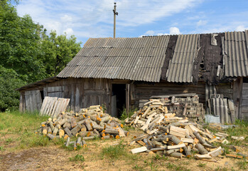 Pile of chopped firewood in village near house. Chopping wood and cutting timber. Preparation of firewood in village for heating house in winter. Old barn in countryside. Rural landscape.