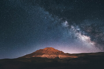Amidst the serene mountains, the milky way paints a cosmic masterpiece against the deep blue night...