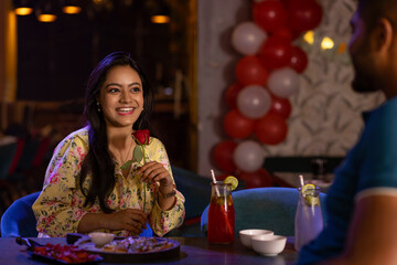 Women with a red rose sitting with her boyfriend at a restaurant