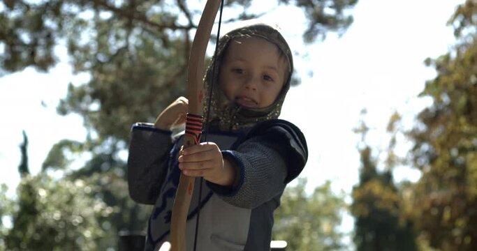 Small boy wearing medieval costume throwing arrow holding bow outside captured in high-speed slow-motion 800 fps