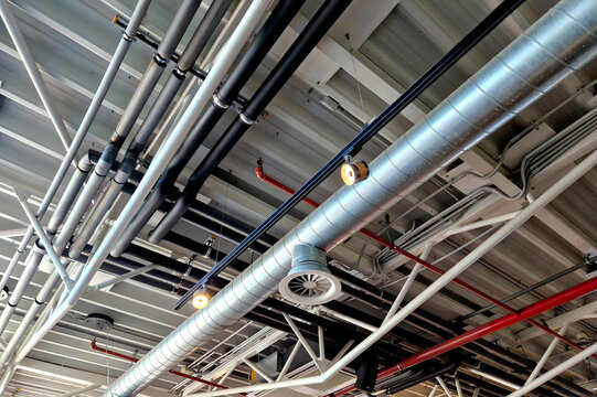 the air handling unit is on the ceiling of the building and is visibly left uncovered. the lights and pipes running under the tin roof give it an industrial feel. whire, suspended ceiling